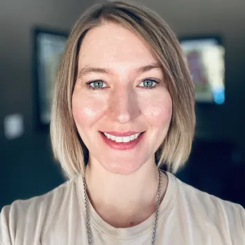 Jaclyn a des cheveux blonds et courts et porte un haut décontracté – elle est photographiée à l’extérieur.
